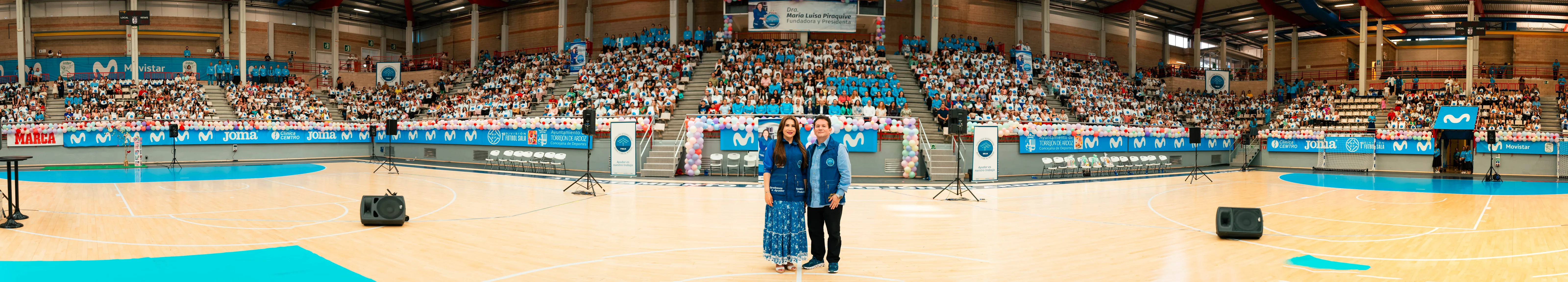 La Dra. María Luisa Piraquive y el Dr. César Eduardo Moreno ante un pabellón lleno de personas durante un evento de la Fundación en España